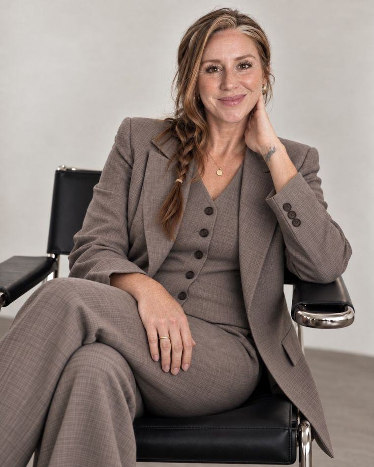 Sonya Heisters seated in a black leather chair, wearing a taupe suit