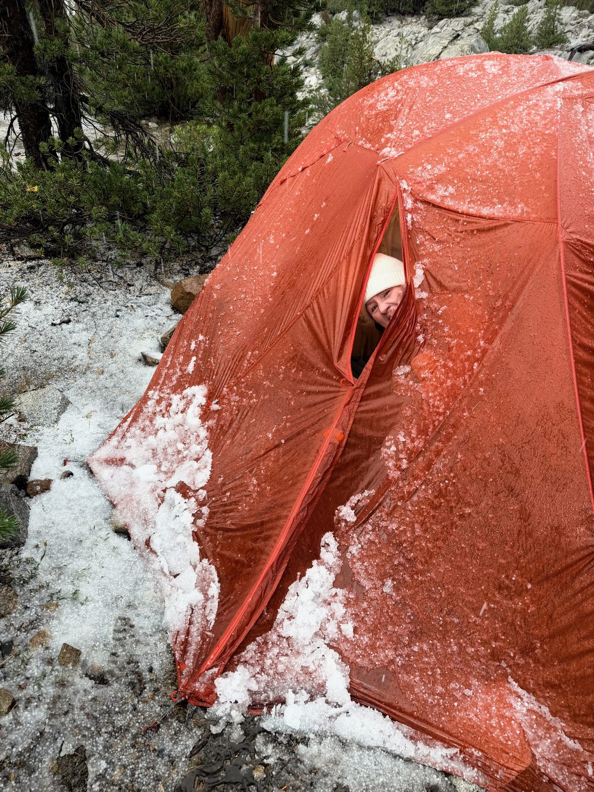 Sonya peeking out of a tent vent, the red tent covered in hail and ice