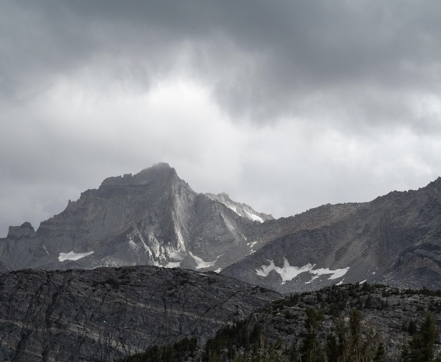 Dark storm clouds hanging low over a granite peak with patches of snow