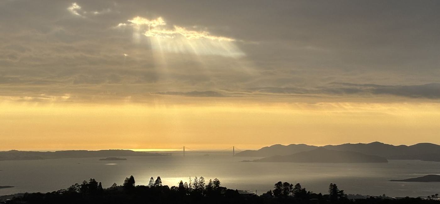 Sunset over San Francisco Bay seen from the East Bay hills, light breaking through clouds above the Golden Gate Bridge