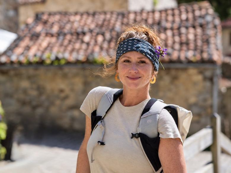 Sonya outdoors on a sunny walk, smiling, with a sprig of purple wildflowers tucked into her headband